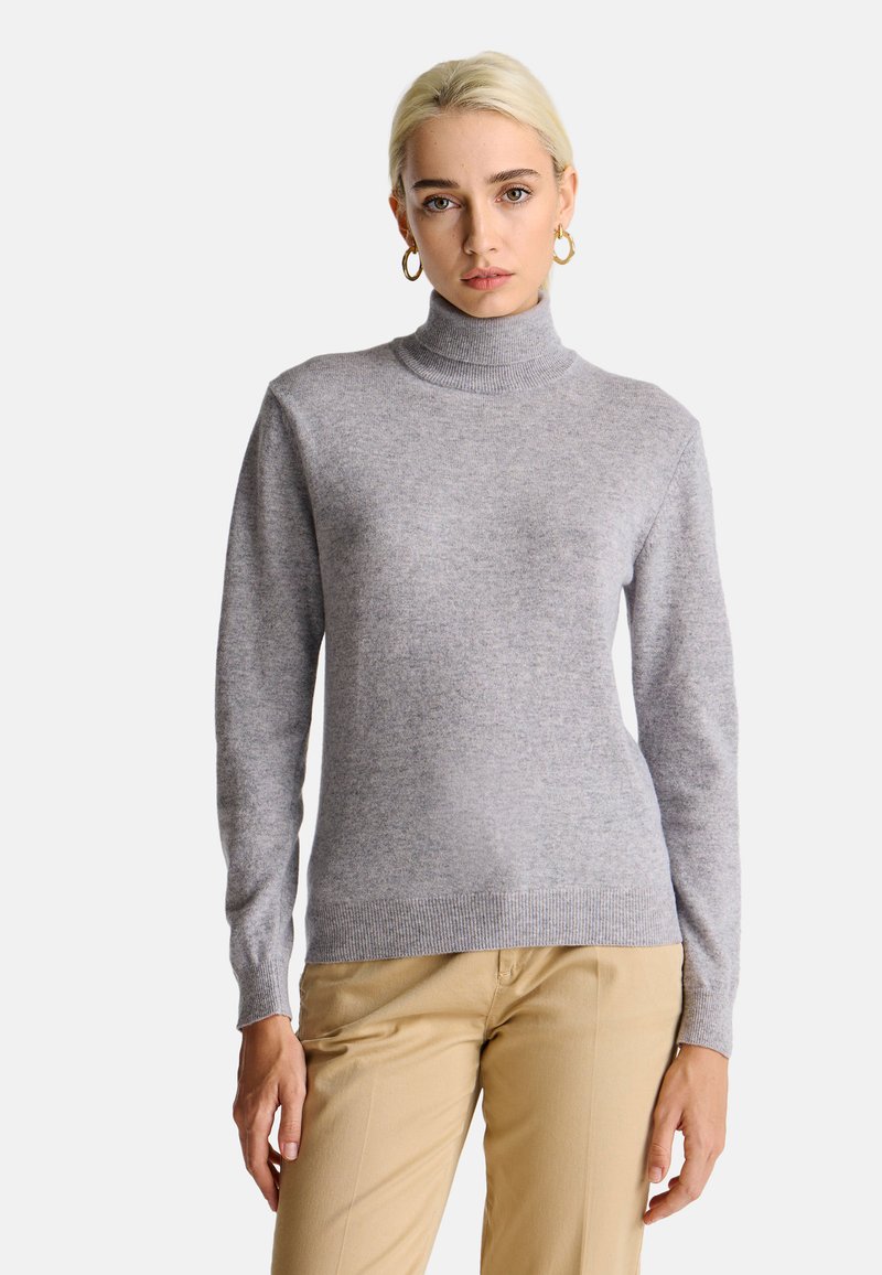 Maglione grigio a collo alto in materiale morbido, con maniche lunghe, polsini a costine e una vestibilità aderente. Abbinato a pantaloni beige.
