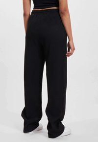 Black wide-leg pants made of ribbed fabric, featuring an elastic waistband. Worn with white sneakers, viewed from the back.