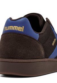Brązowe zamszowe sneakersy z niebieskimi skórzanymi akcentami i złotym logo. Posiadają teksturowaną siateczkę i gumową podeszwę z delikatnym wzorem.