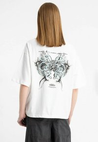 Biała, oversize'owa koszulka z krótkim rękawem, na plecach z szczegółową abstrakcyjną grafiką w odcieniach niebieskiego, czarnego i szarego. Luźny fason.