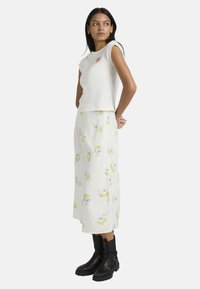 Λευκό αμάνικο τοπ με κόκκινη καρδιά κεντητή, σε συνδυασμό με λευκή midi φούστα με λουλουδάτο μοτίβο σε μπλε και κίτρινες αποχρώσεις. Μαύρα μποτάκια αστραγάλου.