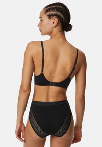 Reggiseno nero con spalline regolabili e chiusura a gancio, abbinato a mutandine nere a vita alta con accenti in pizzo e bordo ondulato.