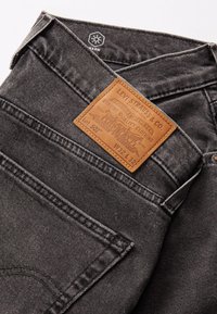 Jeans Levi's 502 din denim gri închis, cu o etichetă din piele maro, cusături vizibile și un design minimalist. Mărimea W32 L32.