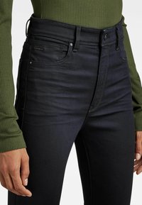 Černé džíny s vysokým pasem vyrobené z denimu, s hladkým povrchem, viditelným švem a předními kapsami. Spárované s žebrovaným zeleným topem.