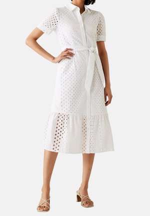 Witte oogjes midi-jurk met korte mouwen, kraag, knoopsluiting aan de voorkant, strikmiddel en volants aan de onderrand, gedragen met beige bandjes haksandalen met blokhak.