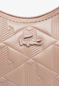 Sac à main en cuir rose avec un motif géométrique embossé, doté d'un logo en crocodile texturé, entouré d'une fermeture éclair dorée.