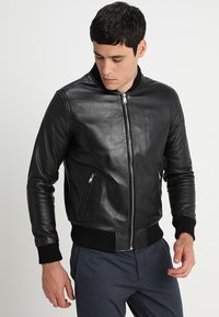 Zwarte leren bomberjack met ribgebreide mouwen en zoom, voorzien van een ritssluiting aan de voorkant en zijzakken. Gladde textuur, klassiek ontwerp.