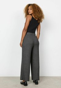 Zwarte mouwloze top gecombineerd met een wijde, heather grijze broek. Gemakkelijk textuur, ontspannen pasvorm en eenvoudig ontwerp. Zwart schoeisel maakt de look compleet.