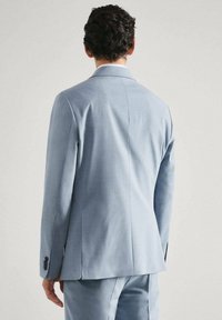 Veste de costume bleu clair avec une coupe ajustée, fente au dos unique et poignets boutonnés. Tissu lisse sans motifs ni ornements visibles.