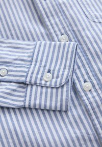 Gros plan sur un tissu de chemise à rayures verticales bleues et blanches avec des boutons blancs et un poignet boutonné.