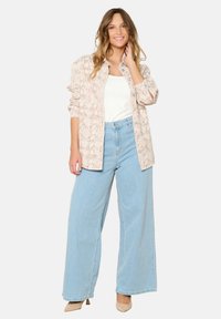 Light pink snakeskin patterned overshirt over a white tank top, paired with high-waisted light blue wide-leg jeans and beige heels.