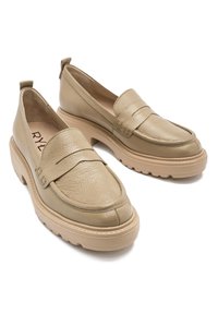 Beżowe skórzane mokasyny z okrągłym noskiem, dekoracyjnym przeszyciem i masywną beżową gumową podeszwą. Z tyłu znajduje się uchwyt ułatwiający zakładanie.