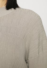 Suéter canelado cinza claro, com gola alta, textura suave e um corte descontraído, apresentando linhas horizontais ao longo do tecido.