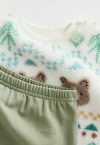 Strukturret cremesvamp sweater med farverige bjørne- og træmønstre, parret med bløde grønne shorts med elastisk talje.