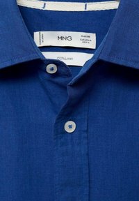 Blauwe linnen shirt met een klassieke kraag, twee knopen en een label dat 100% linnen materiaal aangeeft. Eenvoudig ontwerp met een gladde textuur.