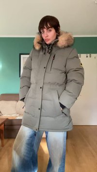 Puhasta siva parka s krznom podstavku, gumbi na pritisak, žepovi sa zatvaračem i elastični manšeti. U kombinaciji s širokim plavim trapericama.