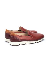 Zapatos rojos tipo slip-on con parte superior de cuero perforado y detalles en cuero color marrón. Presentan una suela crema con un acabado texturizado.