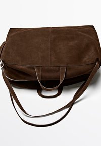 Braune Wildleder-Reisetasche mit doppelten Griffen und einem verstellbaren Schultergurt vor weißem Hintergrund.