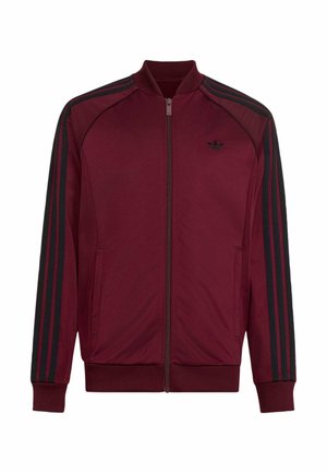 Giacca da ginnastica Adidas color marrone a zip con tre strisce nere sulle maniche e piccolo logo Adidas nero sul petto a sinistra.
