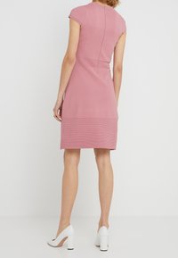 Knee-langes pinkes Kleid mit tailliertem Design, kurzen Ärmeln und strukturiertem unteren Bereich, kombiniert mit weißen High Heels.