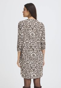 Brūns ziedu raksts kleita ar trim ceturtdaļu piedurknēm, kas izceļas ar zīdainu tekstūru un plūstošu dizainu, garums līdz vidusceļam.