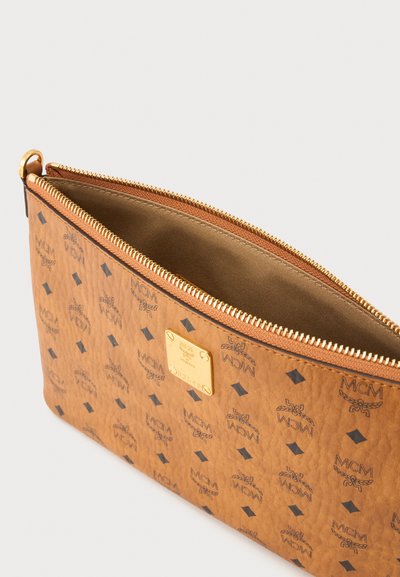 Pochette en cuir marron avec fermeture éclair dorée et plaque logo, décorée de motifs répétés MCM et formes en losange, montrée partiellement ouverte.
