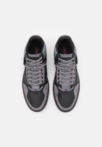 Mustan ja harmaan sekoitusmateriaalista valmistetut lenkkarit, joissa on sileä ja mokkanahkainen tekstuuri, nauhallinen muotoilu ja hillitty logo kielen kohdalla.