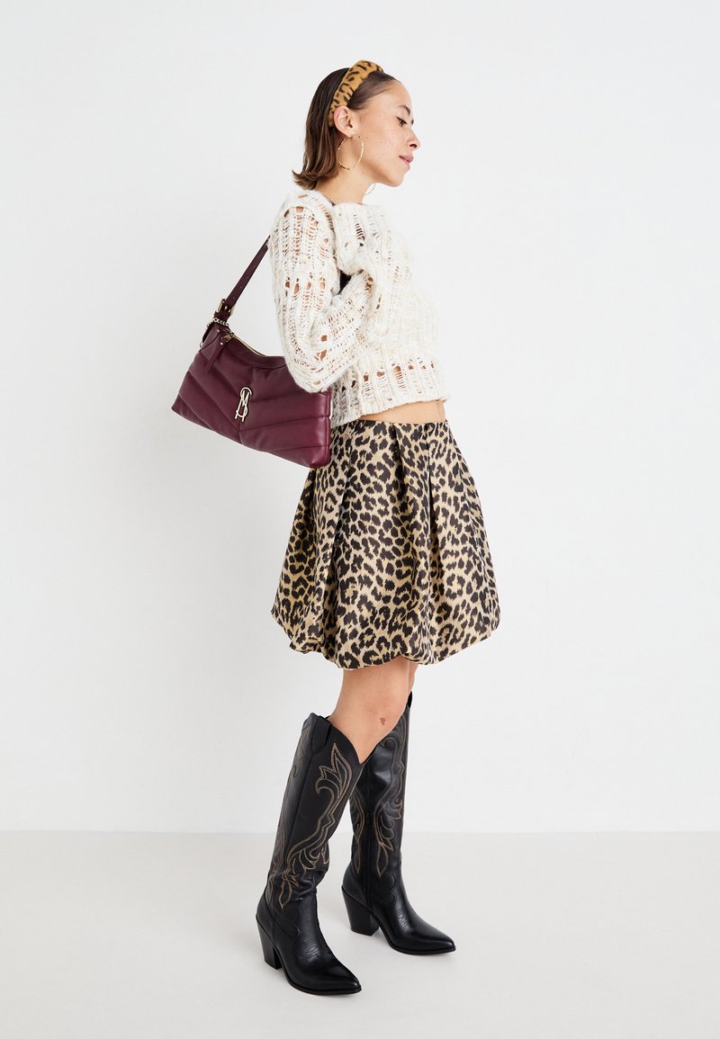 Maglione lavorato a maglia color crema, gonna svasata con stampa leopardata, stivali da cowboy neri con cuciture decorative e borsa a tracolla borgogna.