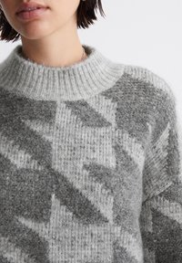 Gray patterned sweater featuring a high ribbed neckline, soft texture, and geometric designs in varying shades of gray.
