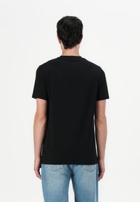 Camiseta negra de manga corta hecha de algodón, con un diseño de cuello redondo. La parte trasera es lisa, sin gráficos ni adornos visibles.
