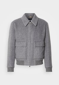Gray herringbone-patterned jacket with a collar, front zipper, and two flap pockets. Features ribbed cuffs and hem for fit.