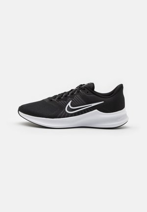 Chaussure de running Nike noire avec un Swoosh blanc et une semelle blanche épaisse, présentée de profil sur un fond uni.