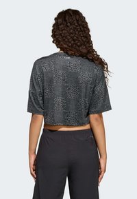 Czarny krótki t-shirt z teksturowanym wzorem w panterkę; krótkie rękawy, okrągły dekolt i luźny krój. Noszony z czarnymi spodniami.