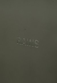 Svart teksturert materiale har et trykket "RAINS"-logo. Overflaten er glatt med en matte finish, som fremhever et minimalistisk design.
