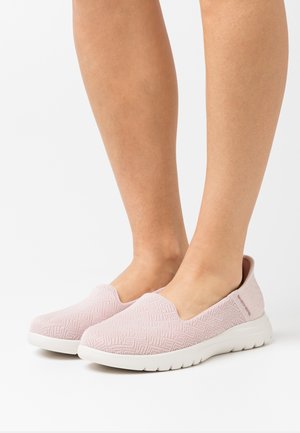 Zapatillas rosa sin cordones con un upper de tejido texturizado, suela blanca y un sutil patrón de espiga. Diseño minimalista sin cordones.