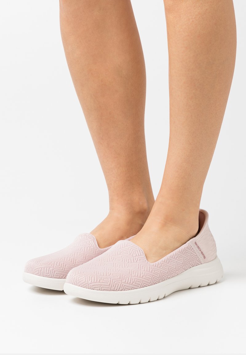 Zapatillas rosa sin cordones con un upper de tejido texturizado, suela blanca y un sutil patrón de espiga. Diseño minimalista sin cordones.