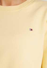 Żółta bluza wykonana z bawełny, z okrągłym dekoltem i długimi rękawami. Małe haftowane logo w czerwonym, białym i niebieskim kolorze na piersi.