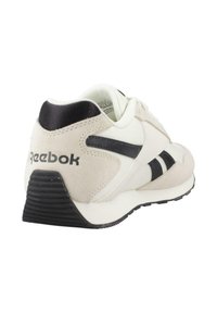 Zapatilla Reebok blanca y beige con logo y detalles en negro, vista desde atrás y de lado sobre un fondo blanco.