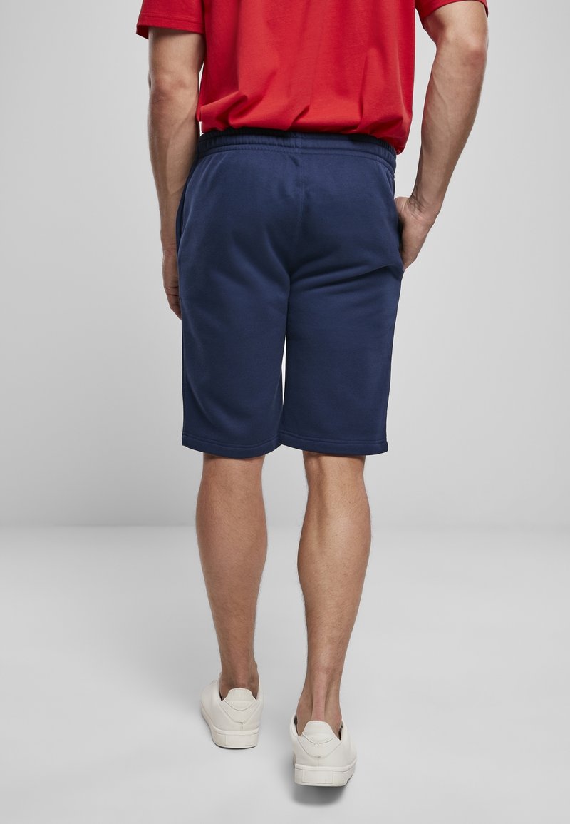 Shorts en coton bleu marine avec une taille élastique, coupé au genou et une texture lisse. Des baskets blanches sont portées.