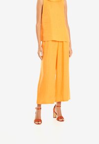 Orange linne topp med rundad halsringning kombinerad med vida orange linnebyxor. Bärs med orange högklackade sandaler med vristremmar.