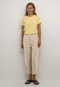 T-shirt en coton jaune associé à un pantalon taille haute beige. La tenue présente une coupe décontractée et est complétée par des sandales noires.