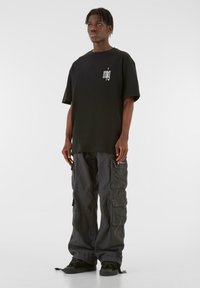 Sort oversized t-shirt med hvidt logo på brystet, parret med mørke cargo bukser med flere lommer og en afslappet pasform. Sorte sneakers.