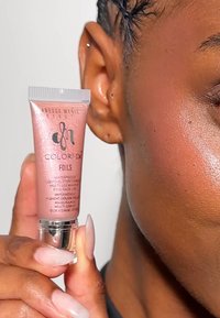 Roze gouden tube met vloeibaar glitterpigment, geperst logo en waterdichte label. Smooth textuur, vastgehouden naast de huid met een neutrale tint.