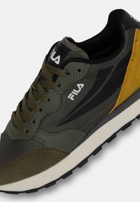 Olivgrüne Sneakers mit schwarzen Akzenten und gelben Details. Hergestellt aus synthetischen Materialien, mit einer strukturierten Oberseite und gemusterten Sohlen.