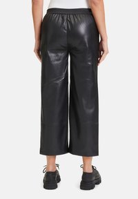 Svart imitationsläderbyxor med vida ben och elastisk midja, med en slät yta och kort längd. Styler med svarta klumpiga skor.