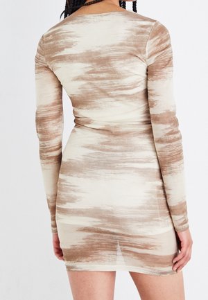 Henkilö, jolla on yllään istuva, pitkähihoinen beigeen ja ruskeaan abstraktiin kuvioon koristeltu mekko, kuvattu takaa punottu hiukset.