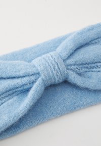 Soft light blue knitted headband with a twisted knot design, showing detailed texture and fibers on a white background.