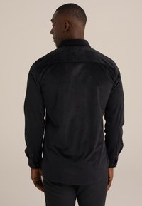 Camisa negra de botón con un patrón texturizado, mangas largas y un cuello clásico. Tejido suave con un corte ajustado.