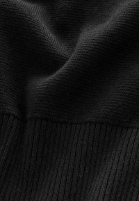 Prim-plan al unui material textil tricotat negru, evidențiind texturi netede și cu nervuri, cu plieri fine și cusături detaliate.