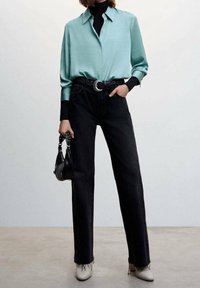 Lys blå, langærmet skjorte; sorte højtaljede jeans; sort bælte med rund spænde; sort håndtaske; cremede sko; slank, moderne design.